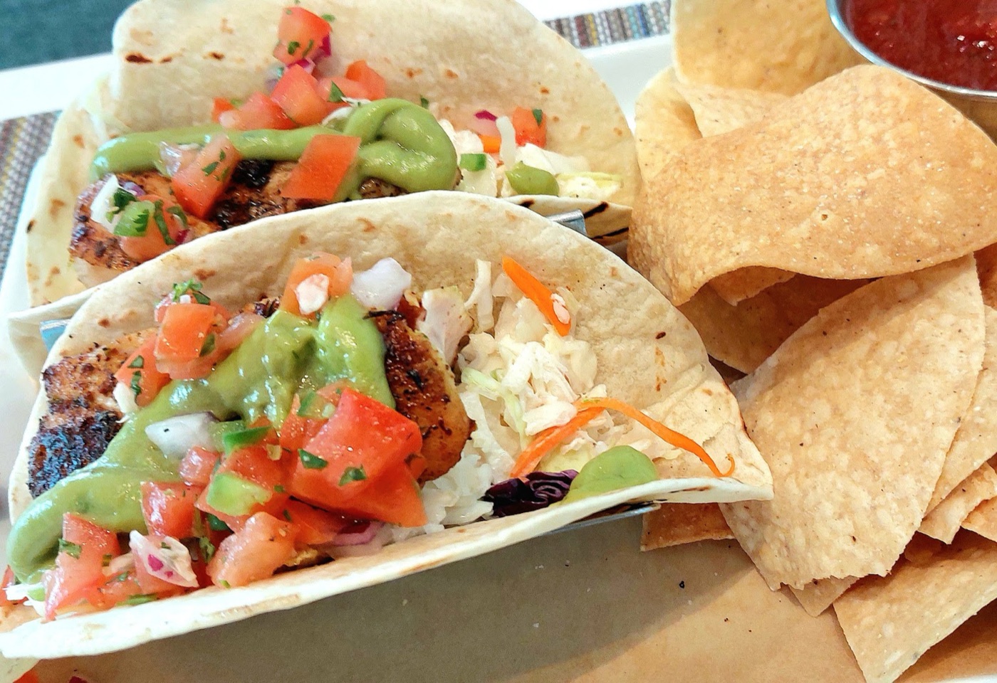 Two blackened fish tacos topped with pico de gallo and avocado crema, with tortilla chips and salsa