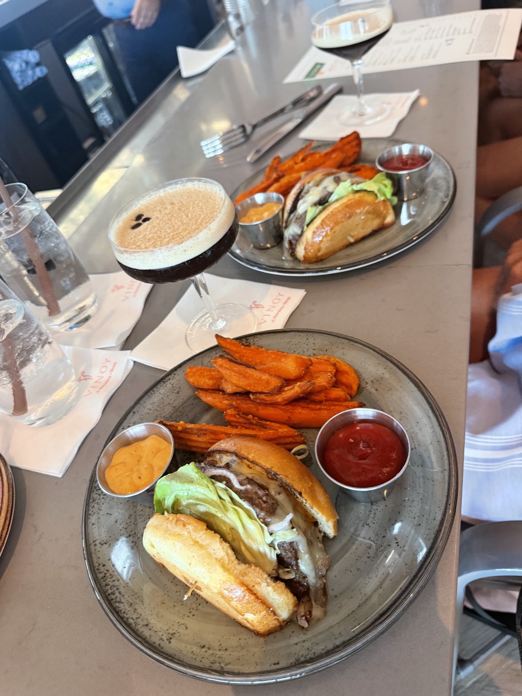 Two cheeseburgers on brioche buns with sweet potato wedges and an espresso martini on the bar counter